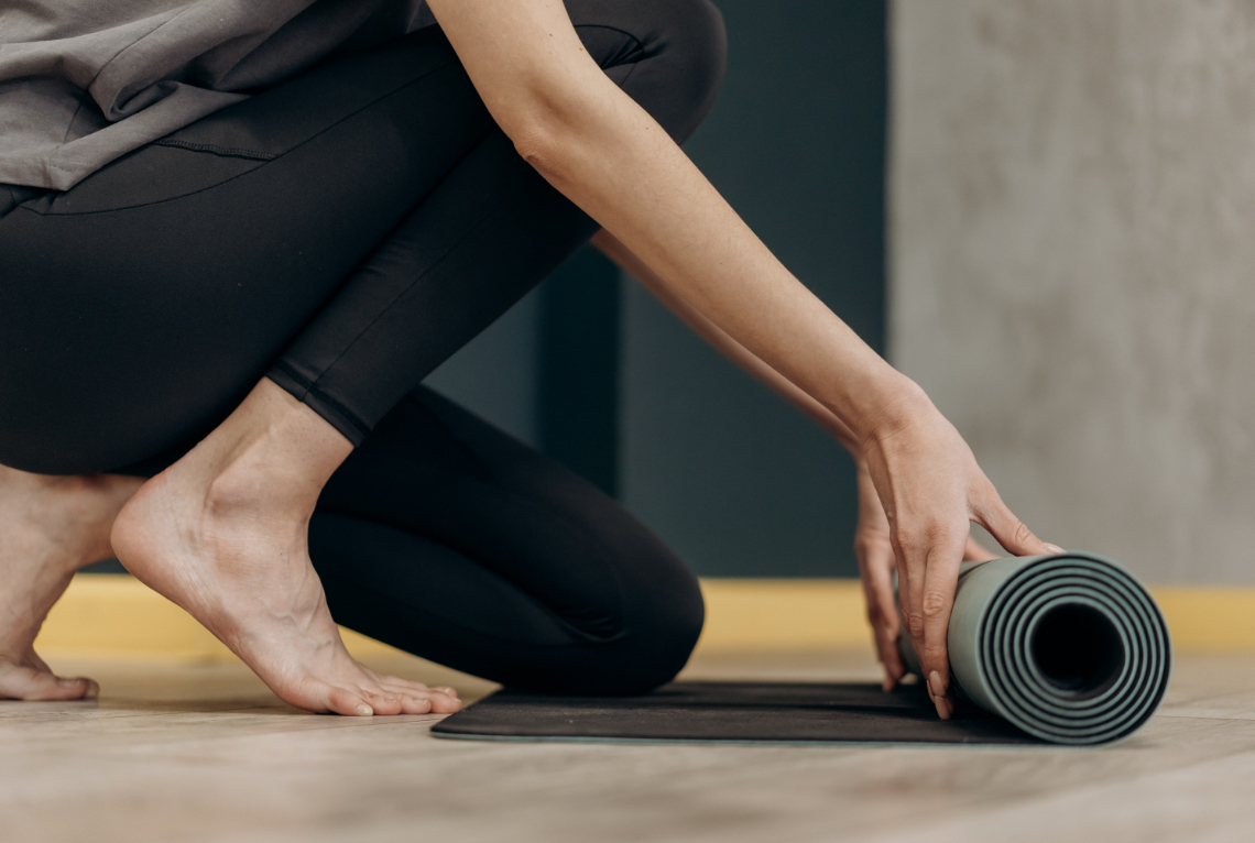 Frau rollt Yogamatte am Boden aus Frau rollt Yogamatte am Boden aus