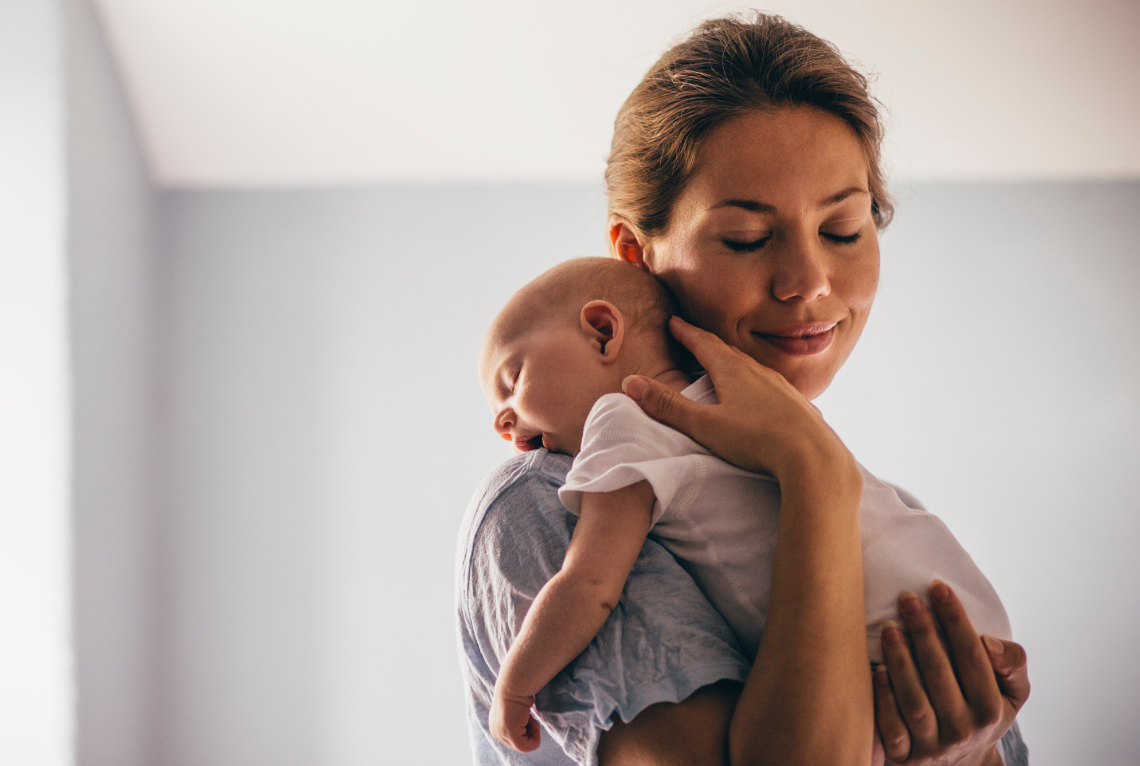 Eine Frau haelt ihr Baby ueber die Schulter und laechelt das Baby gaehnt Eine Frau haelt ihr Baby ueber die Schulter und laechelt das Baby gaehnt