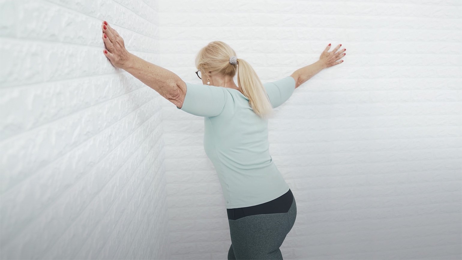Eine blonde Frau an einer Wand macht eine Übung gegen Nackenschmerzen