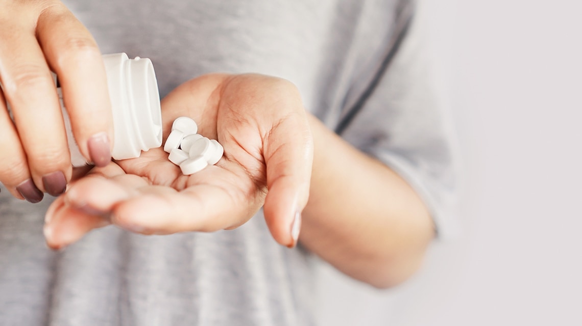 Eine Frau hält schüttet Schmerztabletten aus einer Dose in ihre Handfläche Eine Frau hält schüttet Schmerztabletten aus einer Dose in ihre Handfläche
